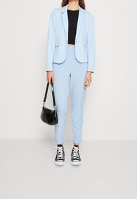 Jasnoniebieska marynarka dopasowana do czarnego topu crop, w połączeniu z jasnoniebieskimi spodniami i czarnymi trampkami. Mała torebka w czarnym kolorze z wzorem krokodyla.