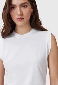 Weißes ärmelloses T-Shirt aus weicher Baumwolle mit rundem Halsausschnitt und glatter Oberfläche, mit leicht umgeschlagenen Schultern für eine lockere Passform.