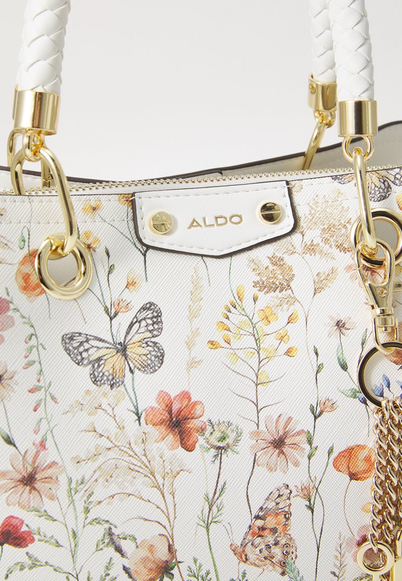 Sac à main à motif floral, en matériau synthétique blanc, avec quincaillerie dorée, anses tressées et des designs détaillés de papillons et de fleurs.