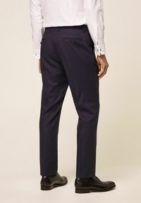 Mornarske hlače izrađene od glatkog materijala, s krojem koji lijepo prati tijelo, sužavajućim nogavicama i stražnjim džepom s gumbom. Uparene s crnim poslovnim cipelama.