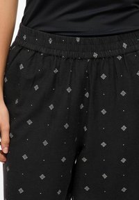 Melni bikses ar elastīgu jostu, rotātas ar baltām ģeometriskām formām un mazām sudraba punktiem, kas piešķir papildus detaļas un tekstūru.