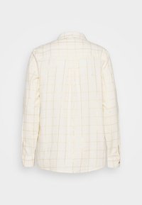 Camicia bianca sporca con un motivo a griglia dorato. Presenta un colletto, maniche lunghe e un orlo dritto. Il materiale sembra texturizzato con cuciture visibili.