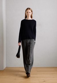 Maglione a coste navy abbinato a pantaloni larghi grigi. La modella porta una borsa nera. Lo sfondo è neutro, con pavimento in legno.