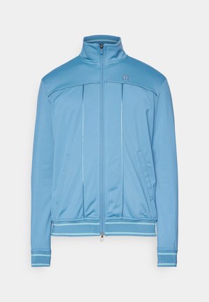 Hellblaue Trainingsjacke mit hohem Kragen, Reißverschluss vorne, seitlichen Taschen und kontrastierenden blauen Bändern an den Ärmelbündchen und dem Saum.