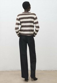 Suéter de punto a rayas marrón y crema con cuello redondo, combinado con vaqueros anchos oscuros y zapatos de tacón alto negros.