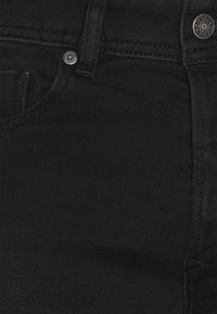 Svarta denimjeans med en slät yta, med en framficka och en metallisk knapp med varumärkeslogo. Minimala sömnadsdetaljer.