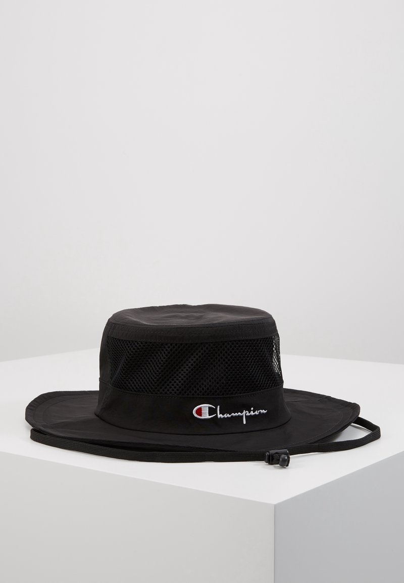 Chapeau bob noir à large bord avec bandes en maille et jugulaire réglable, arborant une broderie du logo "Champion" en blanc et rouge.
