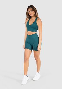 Reggiseno sportivo turchese con scollo a V e design corto, abbinato a pantaloncini a vita alta. Tessuto morbido e strutturato; marchio minimale visibile.