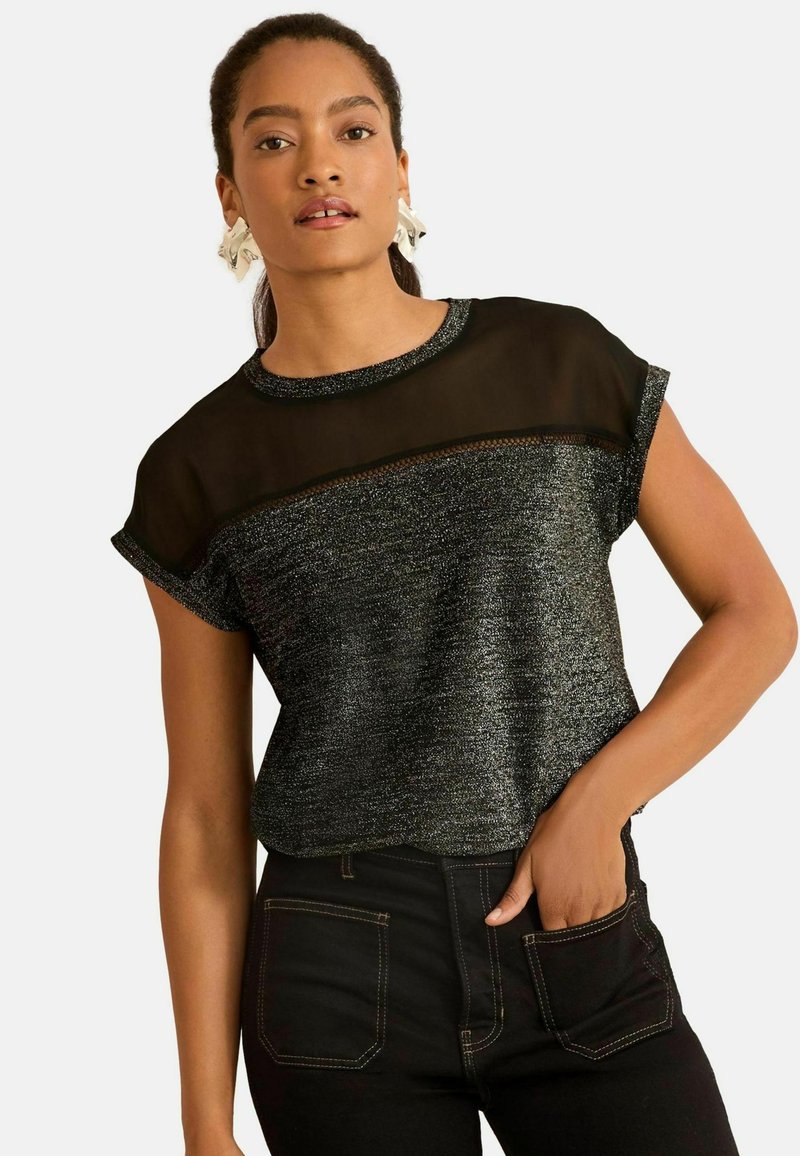 Top corto nero e argento con pannello in rete all' scollo. Tessuto testurizzato con effetto metallico, abbinato a jeans scuri.