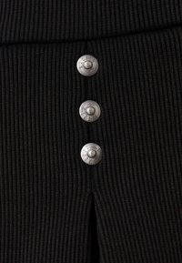 Svart ribbad tyg med tre silverfärgade metallknappar. Texturen är framträdande och framhäver det vertikala ribbmönstret samt knappdetaljerna.