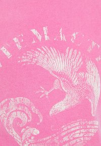 Camiseta de algodón rosa con un gráfico blanco de un pájaro y una ola, con impresión texturizada y letras desgastadas.