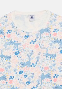 Chemise blanche pour enfants avec un motif de chats bleus et de fleurs roses, bleues et jaunes dispersées sur le tissu.