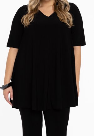 Túnica negra con escote en V y mangas cortas, con un corte holgado y tejido suave. Se lleva con pantalones negros y una pulsera circular.