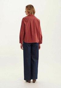 Chemise à carreaux rouge et bleue avec une coupe décontractée et des manches longues, associée à un pantalon en denim large et foncé et des chaussures à talons.