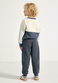 Mikina s blokovými barvami v krémové, světle zelené a námořnické modré barvě, doplněná o odpovídající námořnické kalhoty. Měkká látka s elastickými manžetami. Neformální obuv.