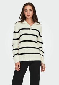 Pull en maille crème avec de larges rayures noires, doté d'un col à demi-fermeture éclair et de manches amples. Texture côtelée et coupe décontractée.