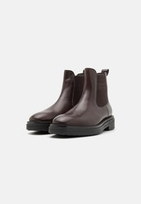 Botas Chelsea de cuero marrón con paneles laterales elásticos y un tirador. Presentan una suela de goma plana y un acabado suave.