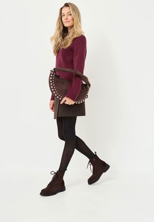 Stivaletti alla caviglia in suede marrone con lacci, un maglione a coste di un intenso bordeaux, e una borsa marrone chiaro con borchie. Collant neri completano il look.