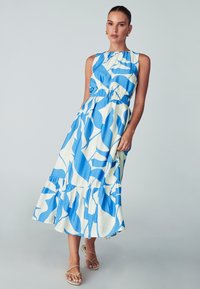Sukienka maxi z niebiesko-białym abstrakcyjnym wzorem, bez rękawów, z elastycznym pasem i falbaniastym dołem. Materiał wydaje się lekki.