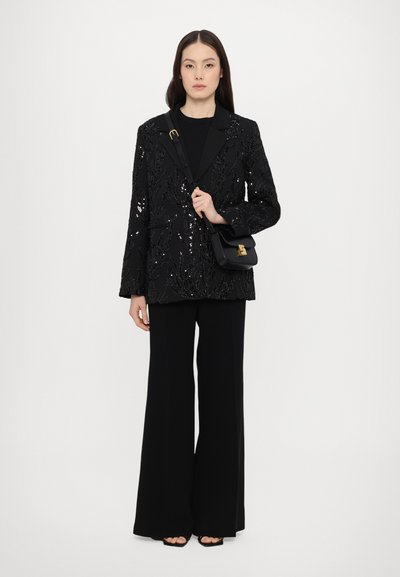 Svart paljettblazer med skreddersydd design, båret over en svart topp og kombinert med løstsittende svarte bukser, holdt med en svart veske.
