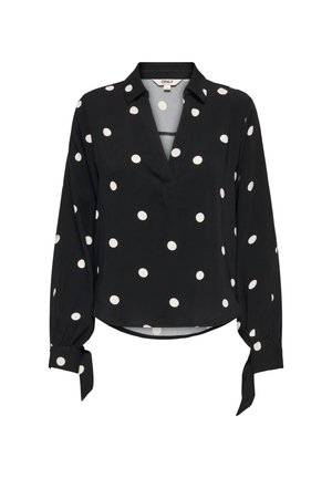 Blouse noire à manches longues à pois blancs, avec un col en V et des poignets noués aux manches.