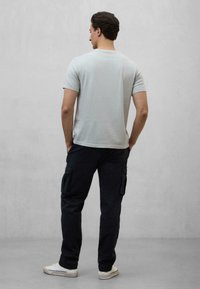 Camiseta de manga corta gris claro, de corte relajado, combinada con pantalones cargo oscuros que tienen bolsillos laterales. El modelo está de pie con las manos en los bolsillos.