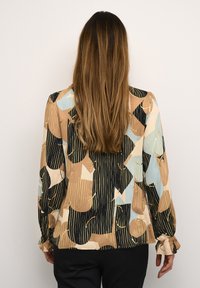 Blusa a maniche lunghe in un tessuto leggero e multicolore con motivi astratti in beige, nero e blu, dotata di polsini arricciati.