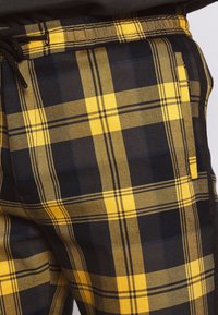 Pantalones de cuadros en negro y amarillo con tela texturizada, cintura elástica y detalle de cordón, que resaltan el audaz patrón de cuadros.