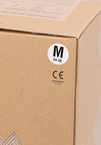 Brun papkasse med et hvidt cirkulært mærke, der angiver størrelse M (54-58) og CE-mærkning, med en tekstureret overflade og enkelt design.