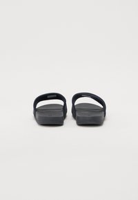 Meripihkan sandal slip-on navy dengan sol karet halus, belakang terbuka, dan sabuk lebar. Permukaan tekstur pada sabuk untuk cengkeraman dan kenyamanan.