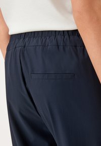 Marineblauwe broek met een elastische tailleband, soepele textuur, voorzien van een enkele paspelzak aan de achterkant, op maat gemaakte design.