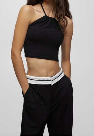 Haut dos nu noir avec une coupe ajustée, présentant un léger éclat. Associé à un pantalon noir taille haute avec une bordure blanche sur la ceinture.
