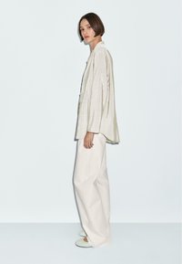 Camicia a righe oversize verde chiaro con maniche lunghe, abbinata a pantaloni bianchi a gamba larga e scarpe slip-on verde chiaro. Design minimalista.