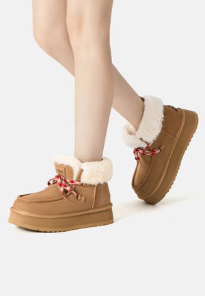 Braune Wildleder-Stiefel mit weißem Futter, roten und weißen gemusterten Schnürsenkeln und einer dicken, strukturierten Sohle. Knöchelhoch mit runder Zehenform.