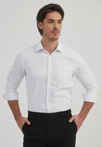 Chemise blanche à boutons avec une poche, manches longues retroussées au niveau des coudes, associée à un pantalon noir. Tissu lisse et design de col classique.