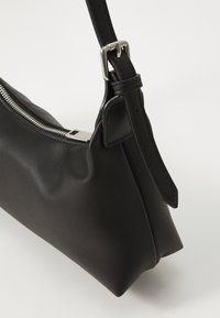 Borsa a spalla in pelle nera con una texture liscia, design sottile, hardware della cerniera argentato e tracolla regolabile. Nota per la sua forma minimalista.