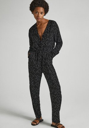 Svart jumpsuit med djup V-ringning, elastisk midja och geometriskt mönster i vitt. Har långa ärmar och sidofickor.