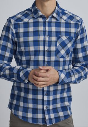 Chemise à carreaux bleue et blanche avec des manches longues, devant boutonné, poche poitrine simple et tissu doux et texturé.