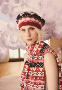 Set di berretto a maglia e sciarpa con motivi geometrici rossi, neri e bianchi, caratterizzato da una texture morbida e una vestibilità aderente attorno alla testa e al collo.