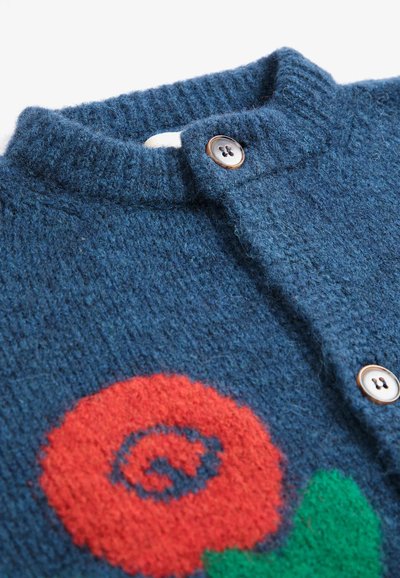 Cardigan en maille bleu avec deux boutons et un motif de fleur rouge avec des feuilles vertes près du bas côté gauche du vêtement.