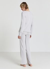 Ensemble de pyjama gris clair en tissu texturé. Comprend des manches longues, un col rond et des bords festonnés. Le pantalon est ample.
