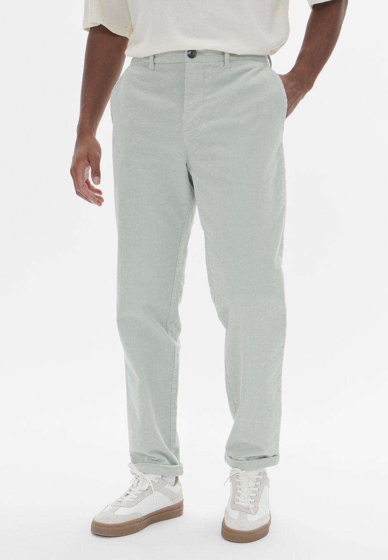 Pantalons droits vert clair en tissu de coton doux. Dotés d'une fermeture à bouton et de poches avant, avec des ourlets retroussés.