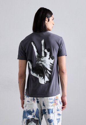 T-shirt in cotone grigio con una grande grafica a mano bianco e nero sul retro. Tessuto morbido con una vestibilità classica, maniche corte.