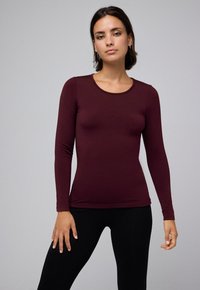 Top burdeos de manga larga hecho de una tela elástica, con cuello redondo y silueta ajustada, combinado con leggings negros.