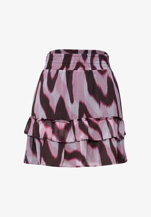 Main d’une femme dans la poche d’une jupe rose, noire et blanche à motifs, avec un volant et une taille élastique, portée avec un haut blanc.