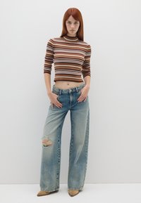 Gestreiftes, eng anliegendes Rippenoberteil in Braun und Beige, kombiniert mit lockeren, hellblauen Jeans, die ein großes Knieloch aufweisen, und beigen spitzen Schuhen.