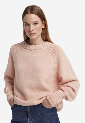 Rosa stickad tröja med rund halsringning, raglanärmar och ribbade muddarna, visas tillsammans med avslappnade jeans i denim. Mjuk textur och ledig passform.