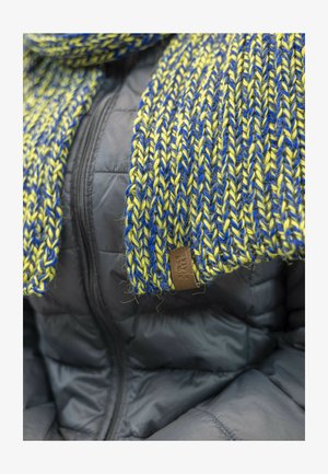 Scarf in maglia giallo e blu, caratterizzato da un motivo testurizzato. Accentuato con un'etichetta in pelle marrone. Indossato sopra un giubbotto nero imbottito.