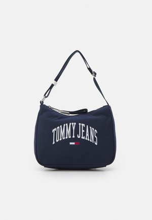 Granatowa torba na ramię z regulowanym paskiem, napisem „TOMMY JEANS” oraz małym czerwono-biało-niebieskim logo z przodu.