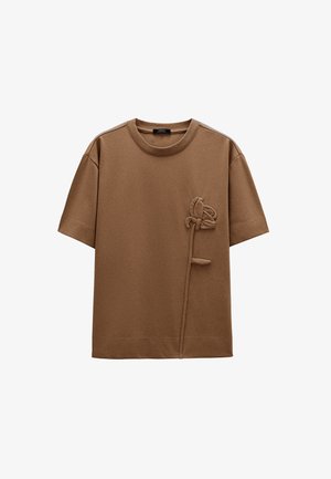 Brązowy t-shirt wykonany z bawełny z teksturowanym, kwiatowym wzorem po lewej stronie, z okrągłym dekoltem, krótkimi rękawami i luźnym krojem.